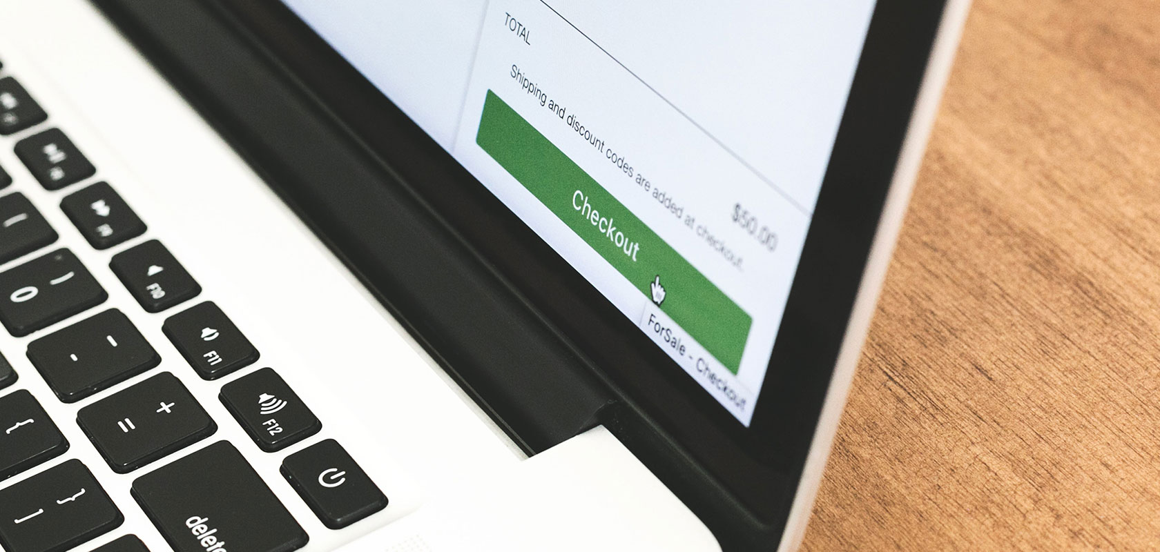 Close-up of a laptop displaying an online shopping checkout page with a "Checkout" button, placed on a wooden surface.