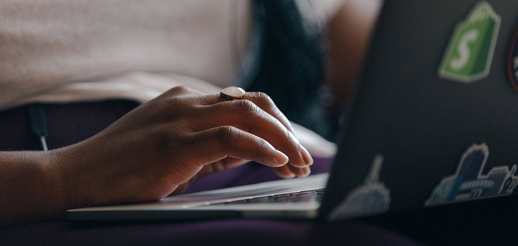 Nahaufnahme einer Person, die auf der Tastatur eines Laptops mit Shopify-Sticker tippt.