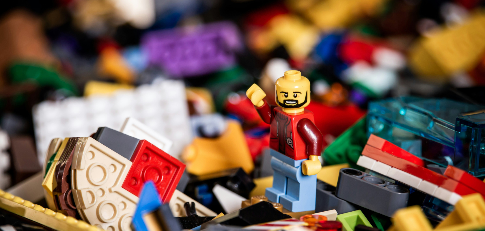 A smiling Lego figure stands amid a colorful pile of assorted Lego bricks and pieces.