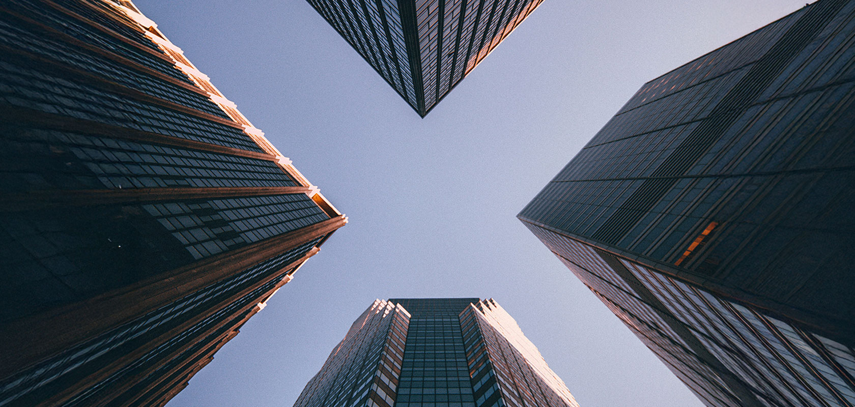 Aufnahme aus niedriger Perspektive von vier modernen Wolkenkratzern, die vor einem strahlend blauen Himmel ein symmetrisches Kreuz bilden.
