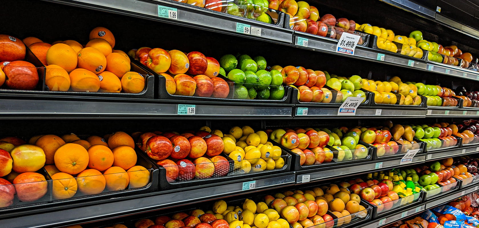 Obst- und Gemüseabteilung eines Lebensmittelladens mit ordentlich angeordneten Kisten voller Orangen, Äpfel, Birnen und Zitronen in den Regalen.