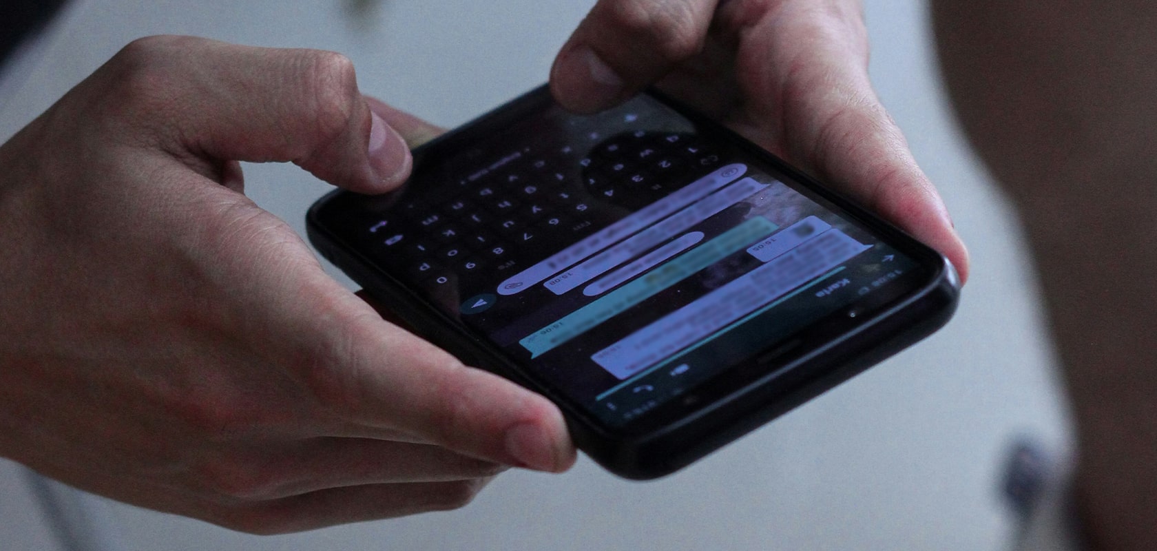 Nahaufnahme von Händen, die ein Smartphone halten, auf dem eine Messaging-App mit Chat-Sprechblasen und einer Bildschirmtastatur angezeigt wird.