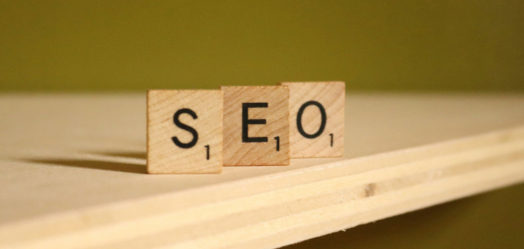 Holz-Scrabble-Steine, die „SEO“ auf einer Holzoberfläche mit grünem Hintergrund bilden.