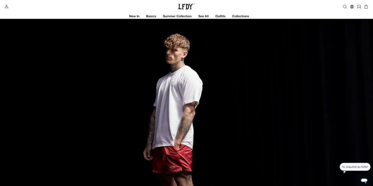 Mann in weißem T-Shirt und roten Shorts steht vor einem schwarzen Hintergrund auf einer Mode-Website.