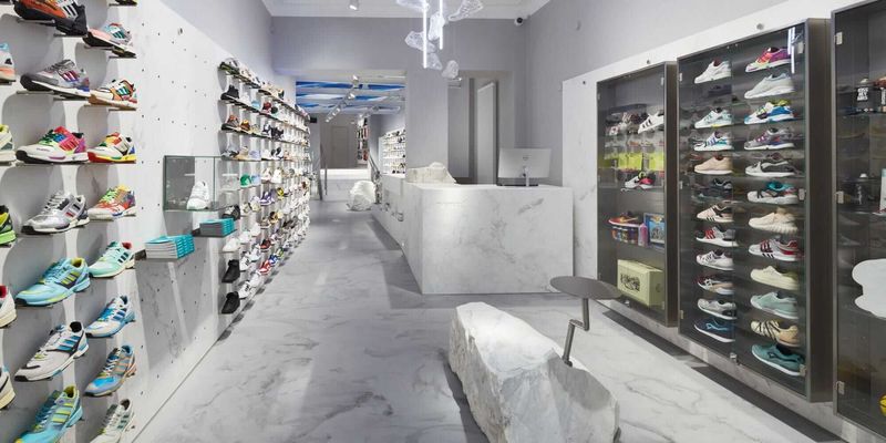 Modernes Sneaker-Geschäft mit weißem Marmorfußboden, schlichten Regalen mit bunten Sneakern und einem minimalistischen Tresen in der Mitte.