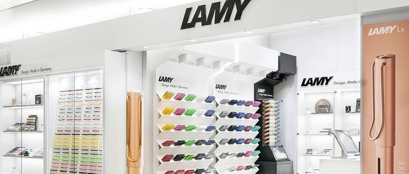 Das Innere eines Lamy-Geschäfts mit bunten Stiften in Regalen und Markenschildern. Auf der rechten Seite ist ein großes Stiftmodell zu sehen.