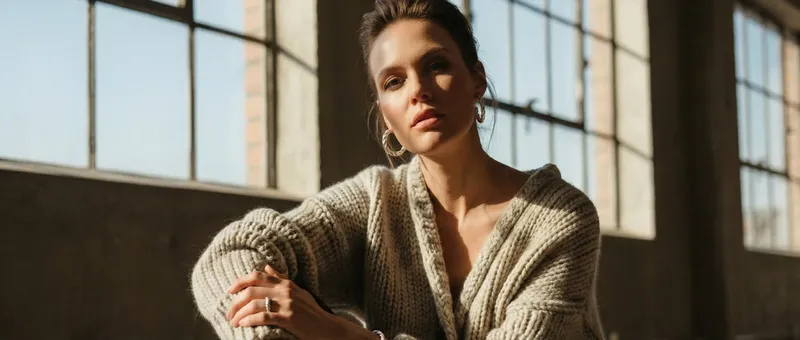 Eine Frau in einem kuscheligen Strickpullover sitzt in der Nähe großer Fenster, die sanft von Tageslicht beleuchtet werden.
