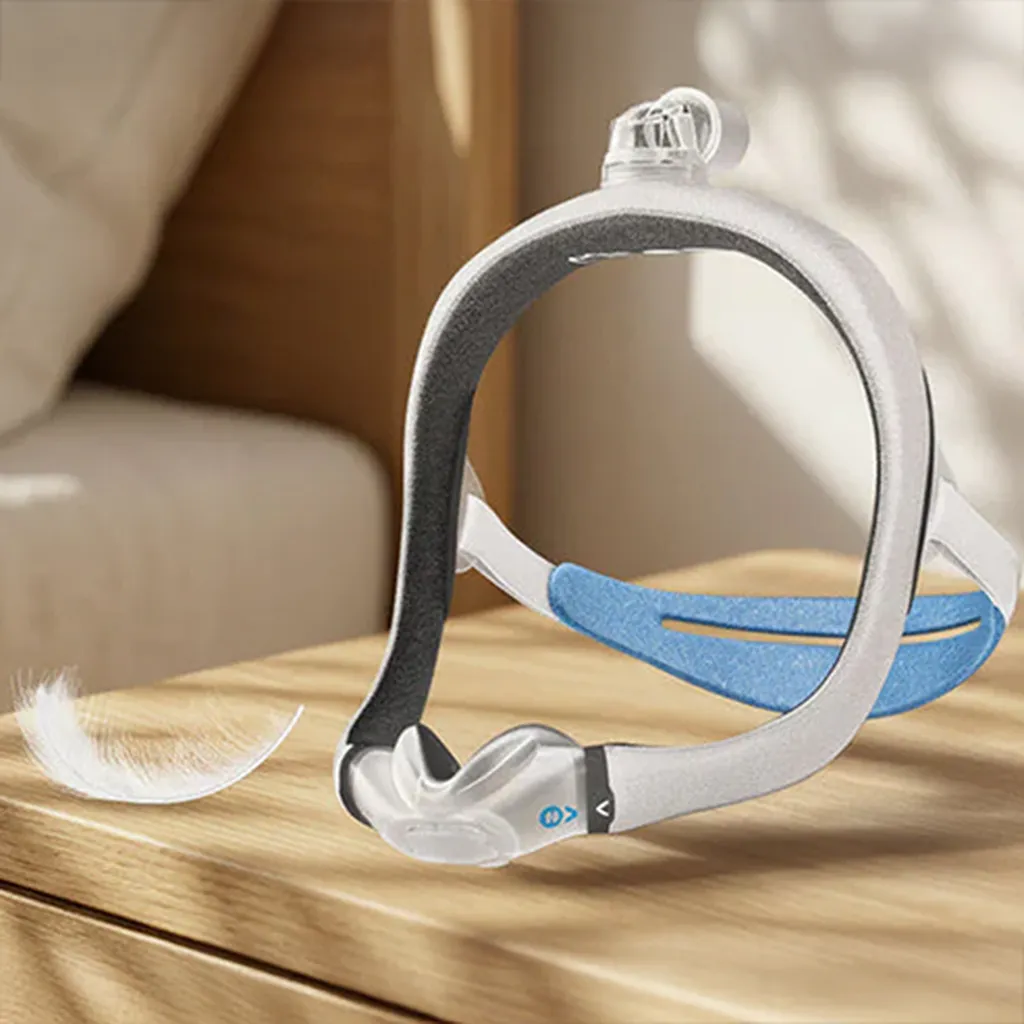 Leichte CPAP-Schlafmaske mit Kopfband auf einem Holztisch neben einer Feder.