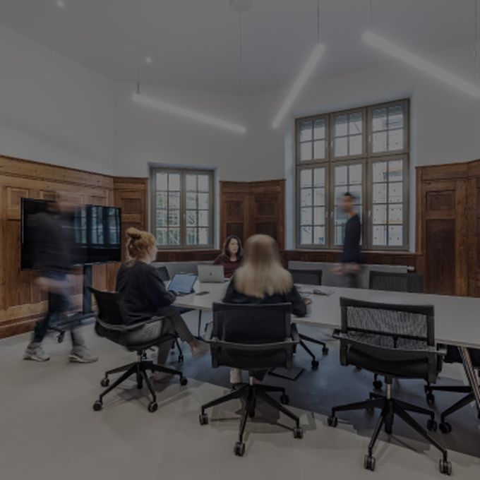 Dynamisches Meeting im Gründerzimmer, Personen in Bewegung und Diskussion am Tisch