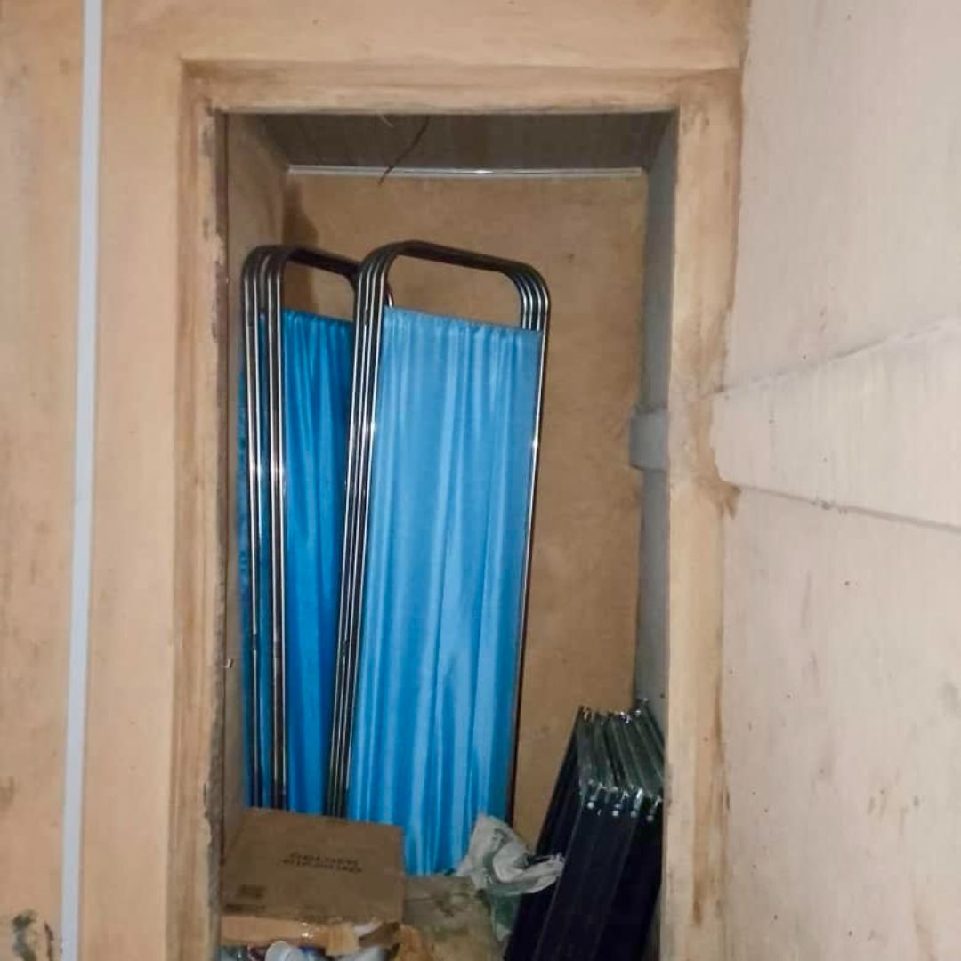 A narrow storage space with two folded blue privacy screens and a cardboard box on the floor. Walls are unfinished and beige.