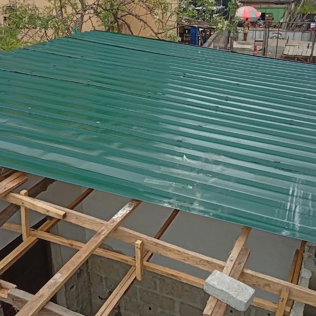 Green corrugated metal roofing sheets installed over a timber framework structure at a building construction site.