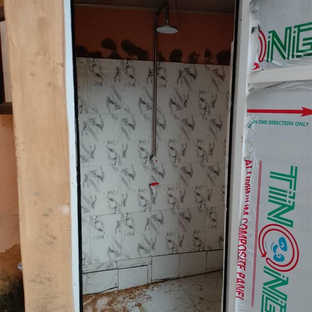 A partially constructed shower area with floral-patterned tiles and an exposed showerhead, surrounded by unfinished walls and packaging material.