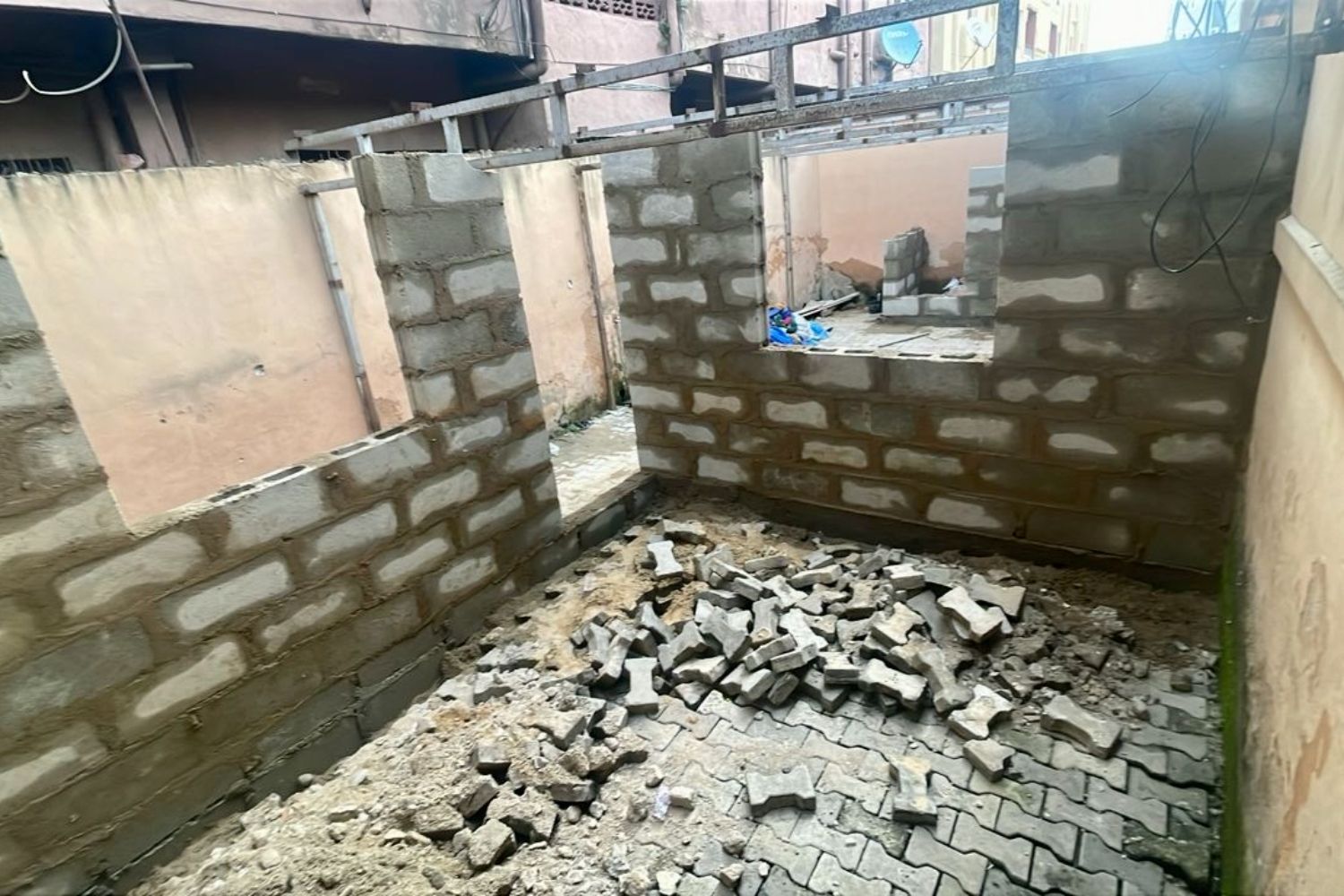 Partially constructed room with brick walls and two window openings, debris and paving stones scattered on the ground.