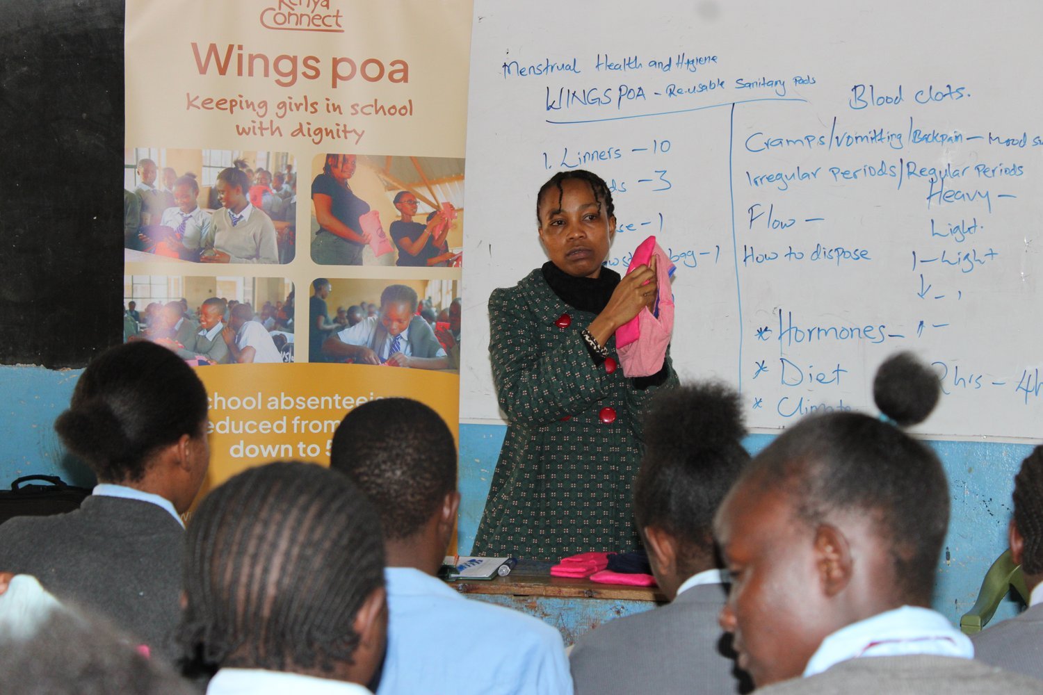 A woman holding a reusable sanitary pad presents a menstrual health and hygiene lesson to students in a classroom.