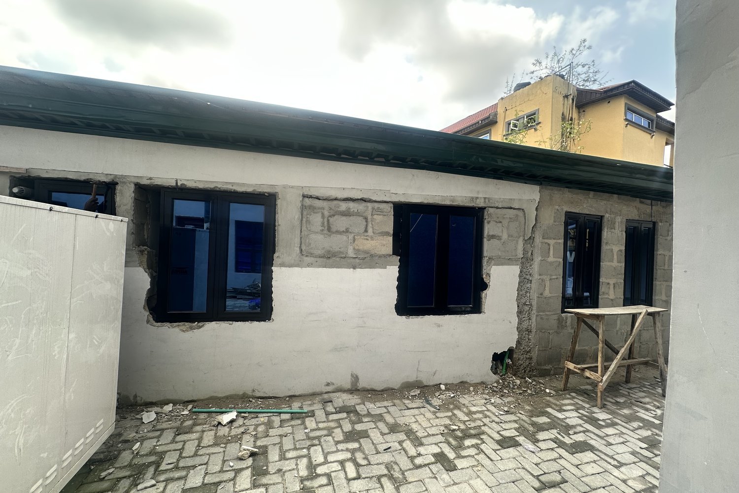 A single-storey building under renovation with dark-framed windows set into unfinished grey concrete block walls on a cobblestone courtyard.