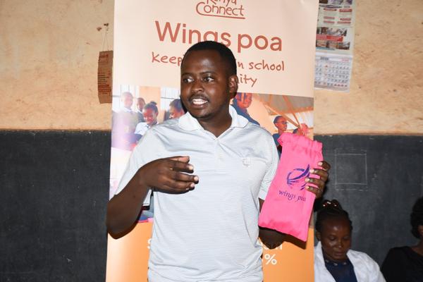 A man in a grey polo shirt holds a pink WingsPoa branded bag in front of a Kenya Connect banner.