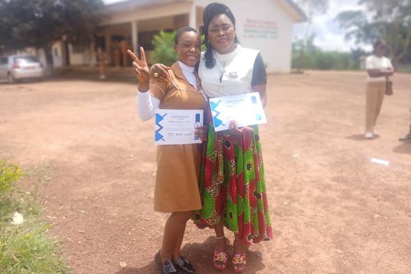 Two graduates hold their certificates outdoors after the ceremony, one making a peace sign.