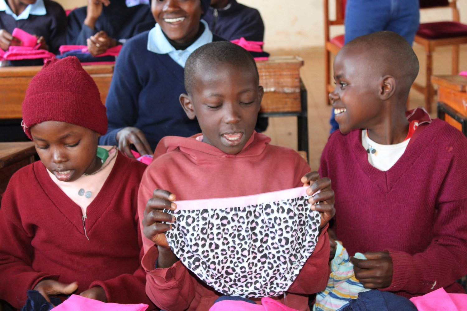 Children in red uniforms examining underwear whilst seated in a classroom with wooden desks.