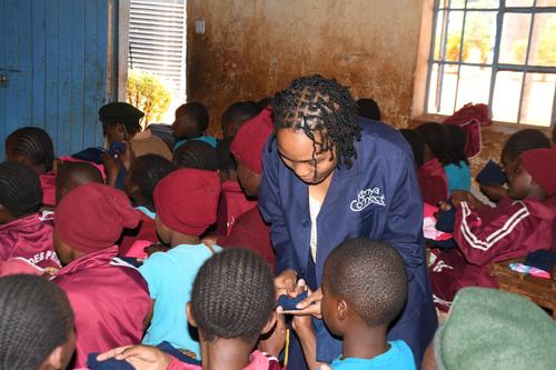 A Kenya Connect worker distributes kits to uniformed schoolchildren in a crowded classroom.