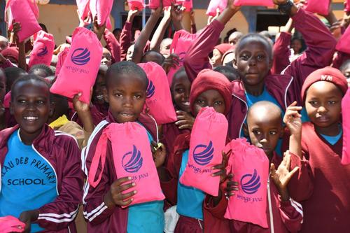 Children in maroon uniforms hold pink WingsPoa drawstring bags outdoors at school.