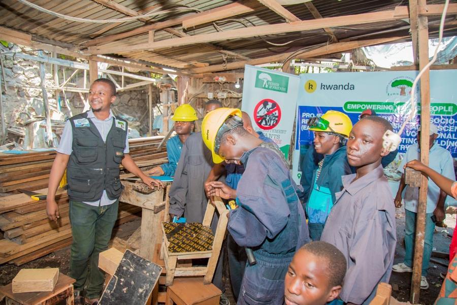Young people in hard hats practising carpentry in a workshop stacked with lumber.