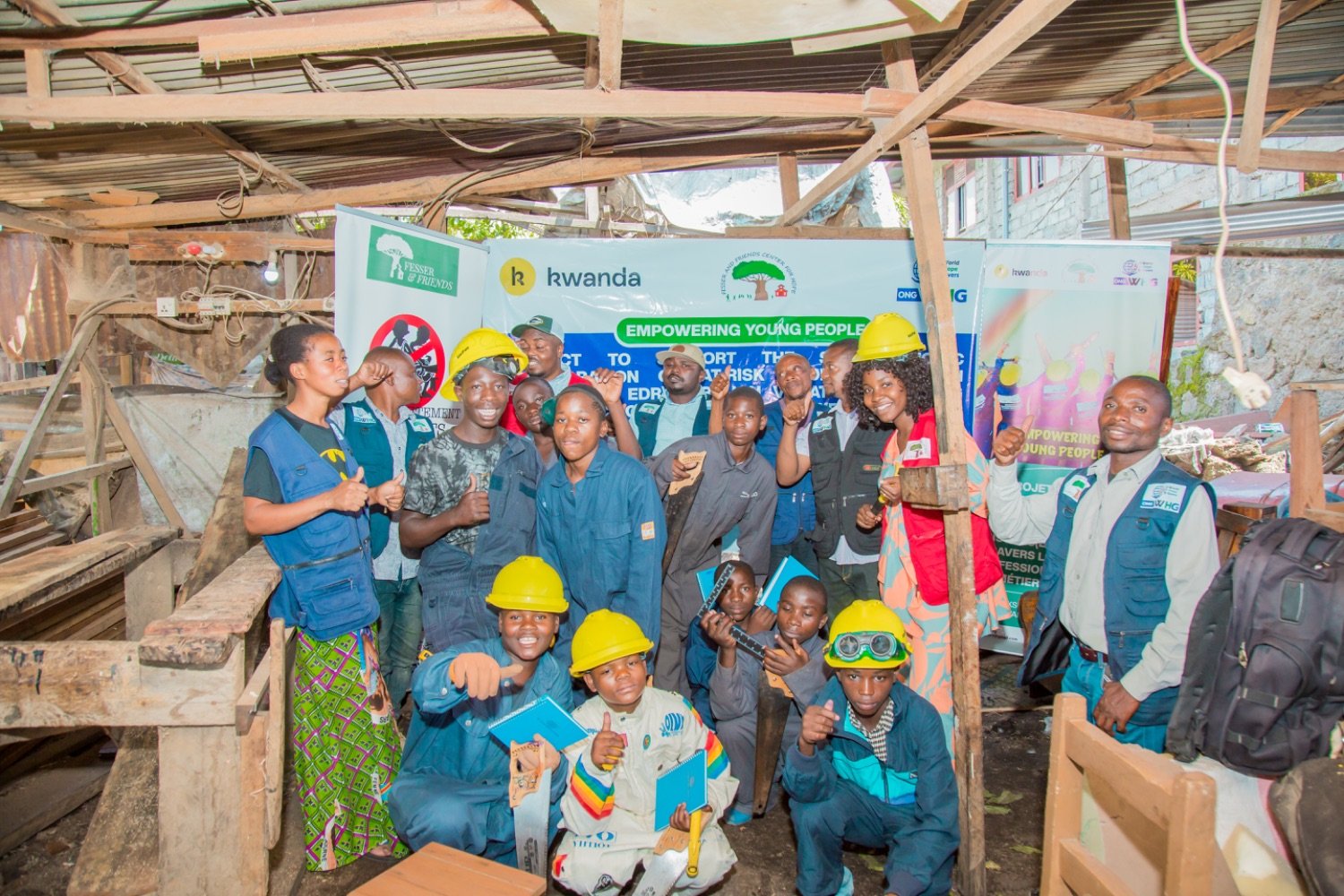 Young people in hard hats and blue work uniforms posing together in a workshop under an "Empowering Young People" banner.