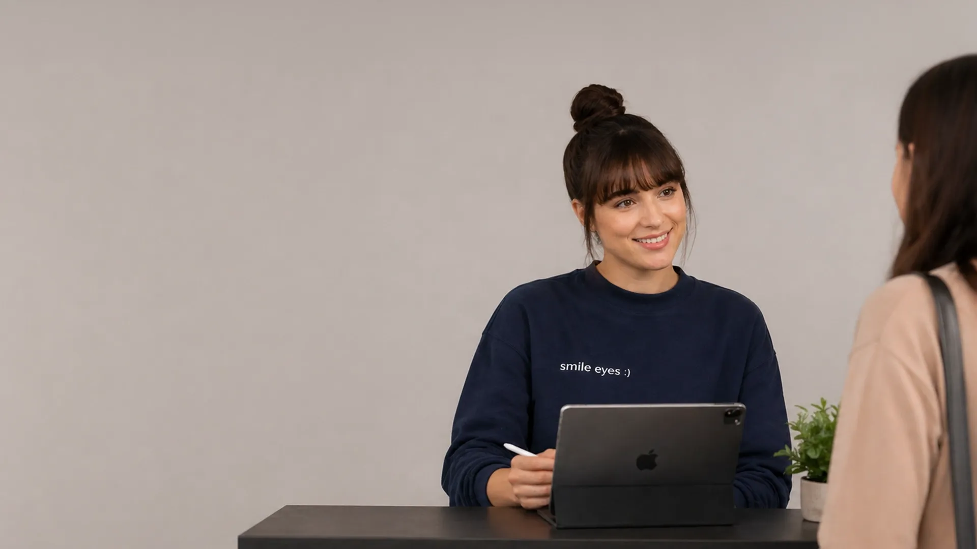 Eine lächelnde Kundendienstmitarbeiterin mit Headset und einem T-Shirt mit der Aufschrift „Smile Eyes“, die vor einem grauen Hintergrund an einem Laptop sitzt.