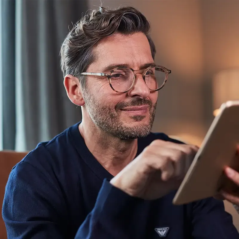 Mann mittleren Alters mit Lesebrille nutzt ein Tablet – Symbolbild für die Ursachen der Alterssichtigkeit.