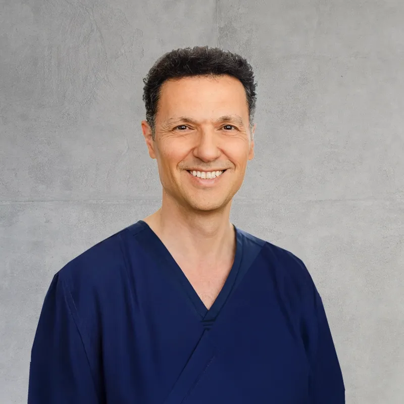 Smile Eyes Augenarzt Dr. Suphi Taneri aus Münster steht lächelnd vor einem unscharfen Hintergrund.