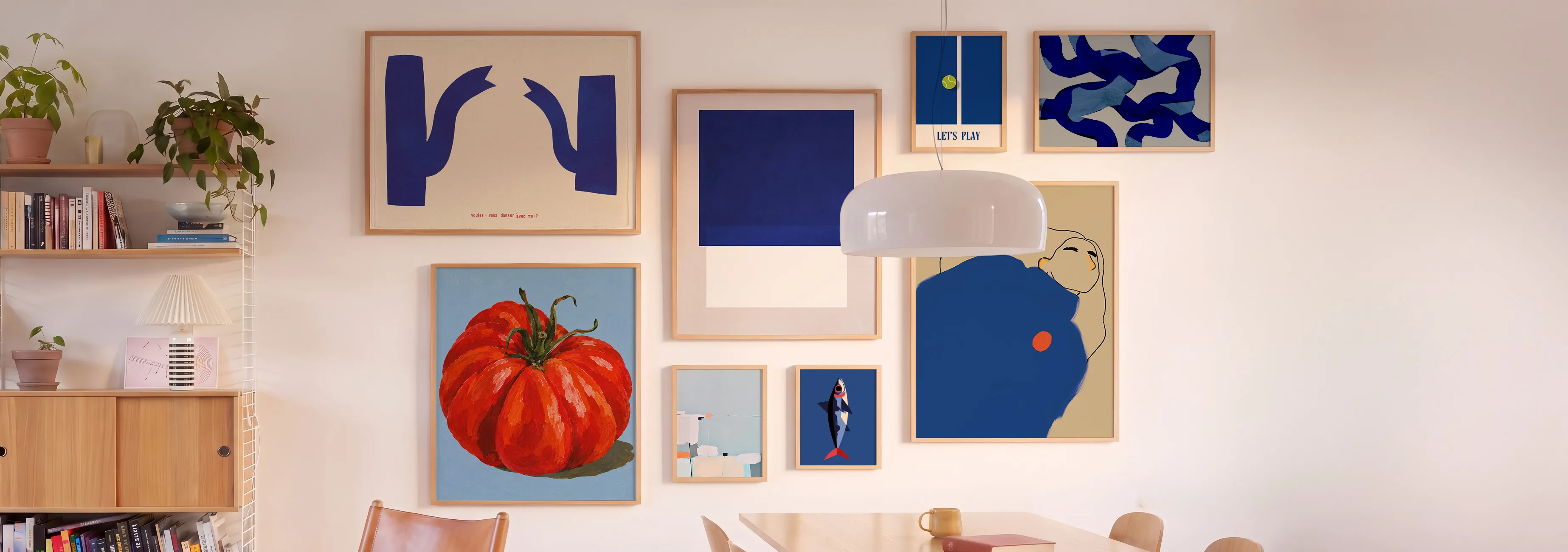 A dining room wall decorated with colorful abstract art, a plant, bookshelves, and a modern pendant light above a wooden table and chairs.