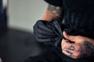 Person mit Tätowierungen, die schwarze Handschuhe trägt und sie mit den Händen zurechtrückt.