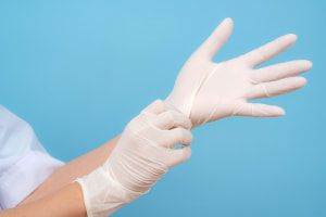 Person, die weiße Einmalhandschuhe vor einem blauen Hintergrund anzieht.