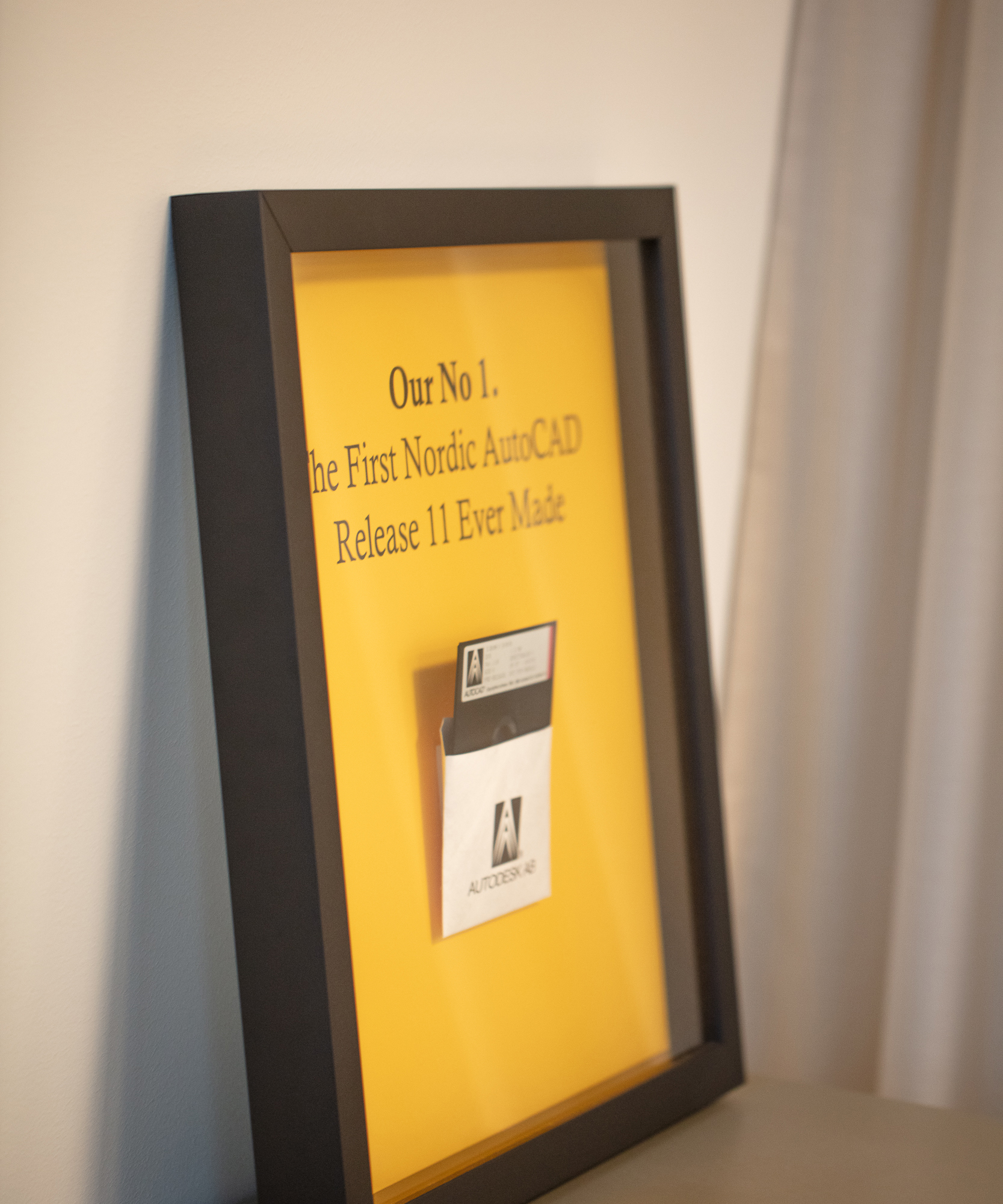 Framed display of the first Nordic AutoCAD Release 11 disk, with a yellow background and black text highlighting its significance.