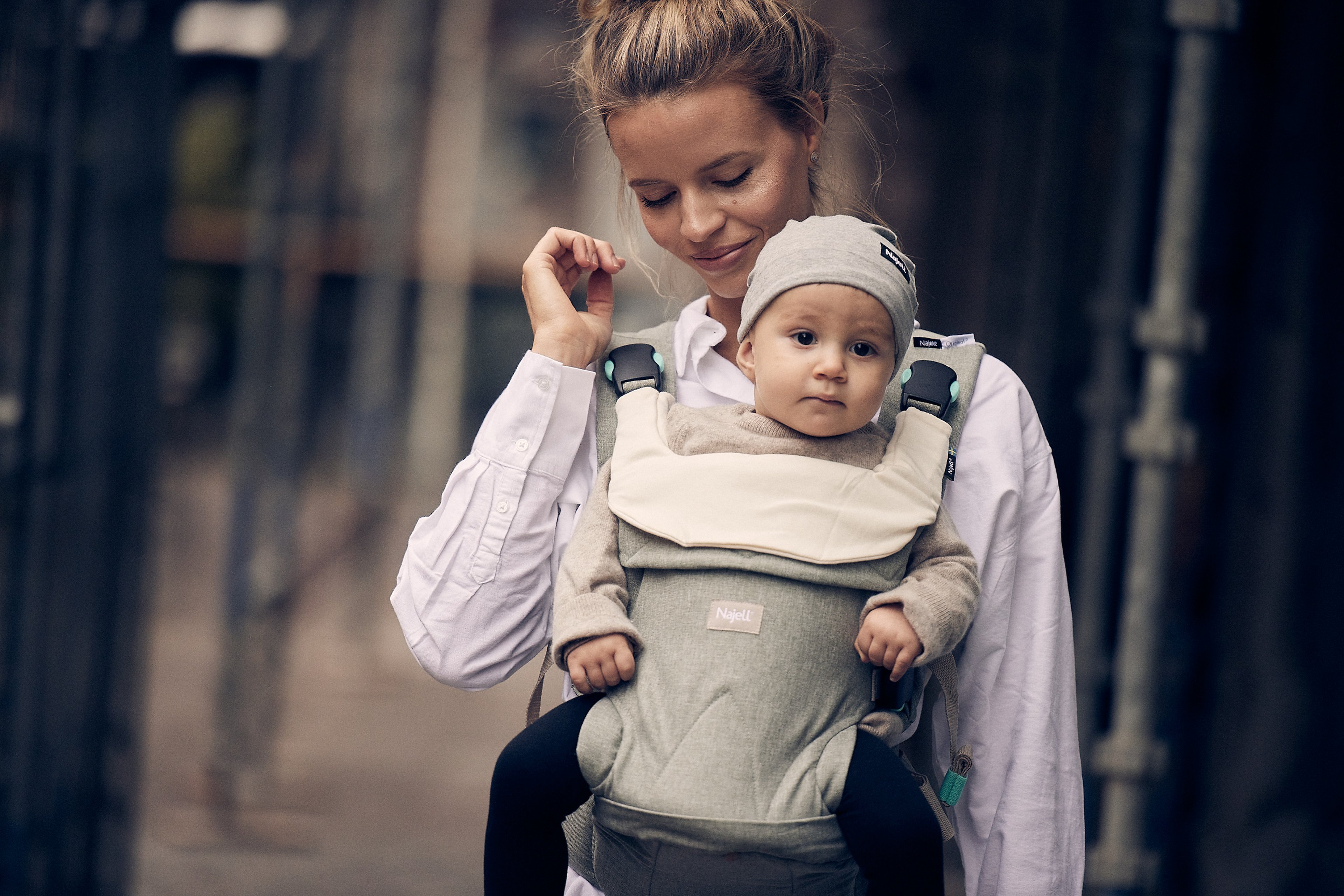 Woman walking carrying a baby in a Najell Original sage green baby carrier