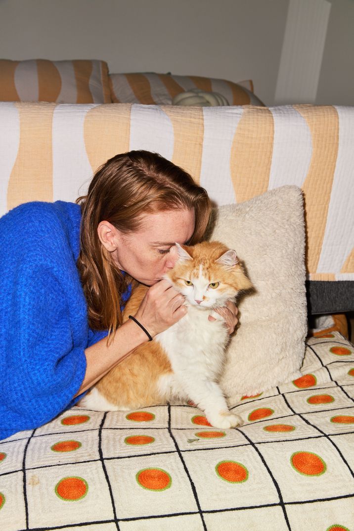 Woman cuddling her ginger and white cat, giving him head kisses.