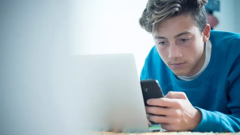 adolescente em frente ao notebook verificando seu celular