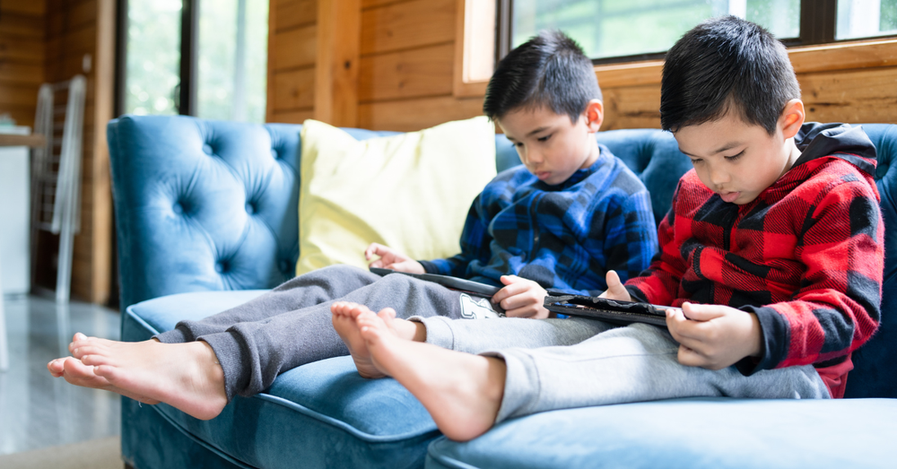 Zwei kleine Jungs sitzen auf dem Sofa und starren in ihre Tablets