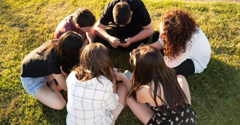 criancas sentadas num circulo cada uma com seu celular na mao