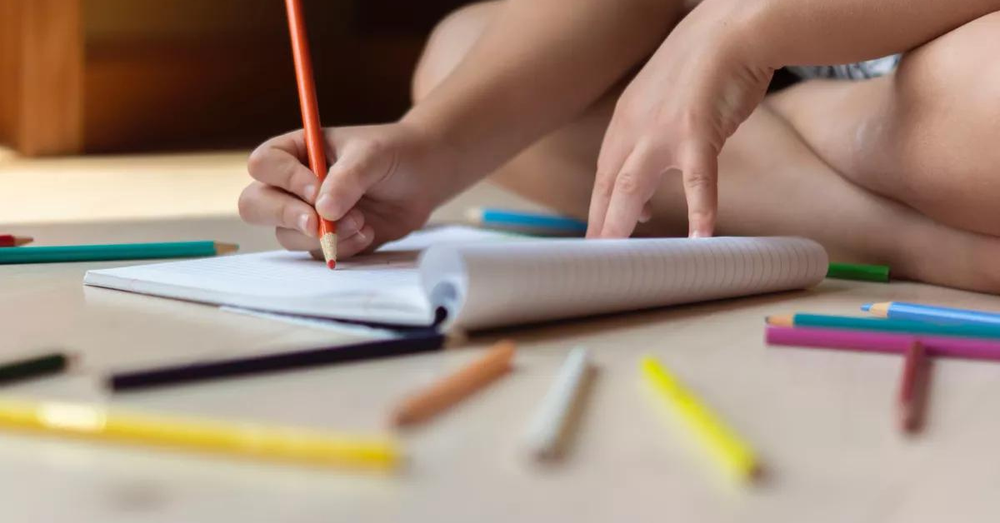 criança pintando com lápis de cor um caderno sentada no chao