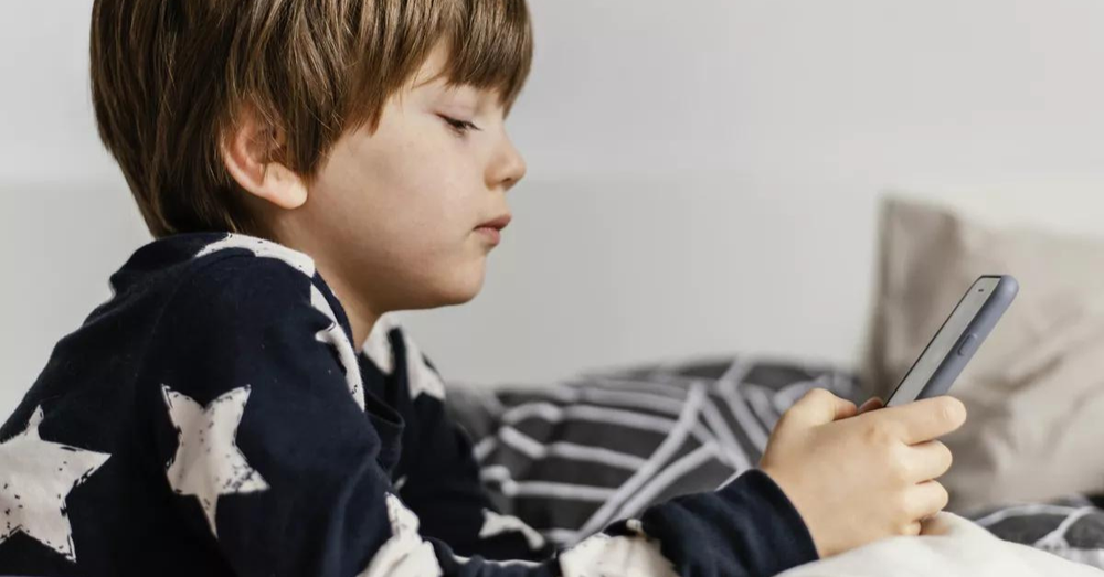 menino com deitado na cama mexendo no celular