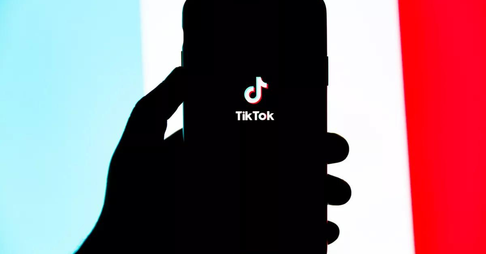 sombra de uma mão segurando celular com a logo do TikTok no centro