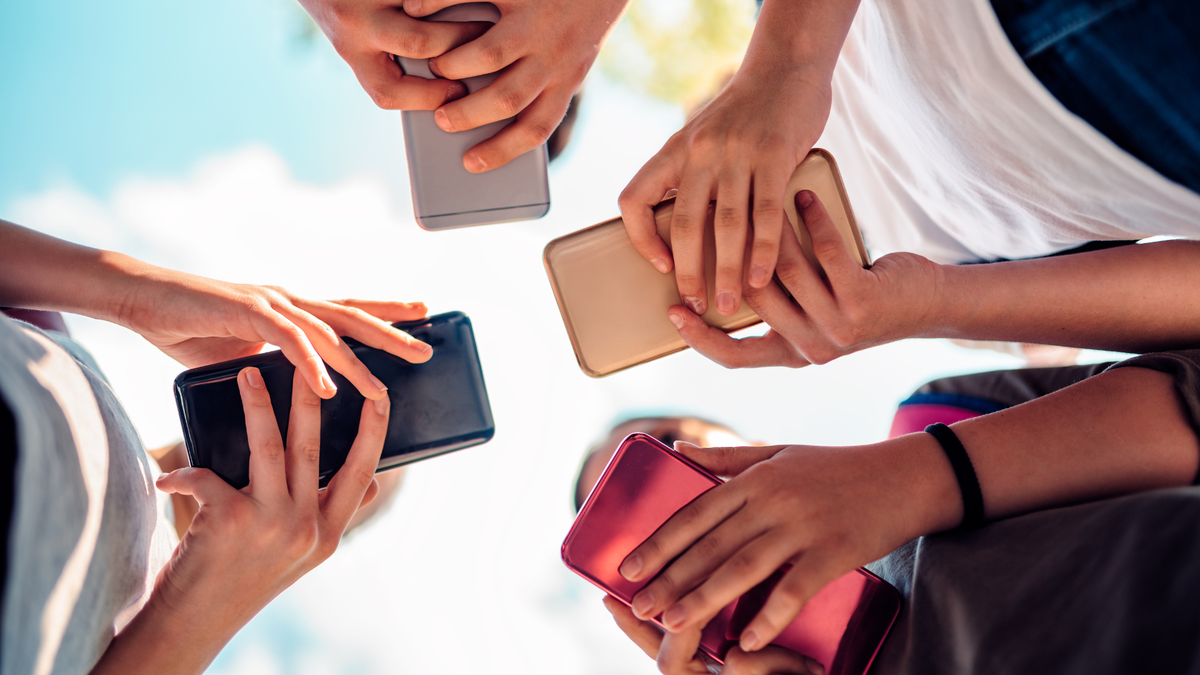 Four kids holding their phones, photo was taken from the bottom up so you see the back of the phones