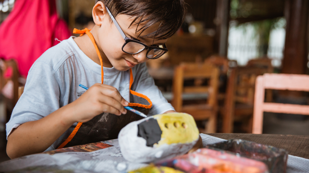 boy with glasses is painting his self-made paper bus