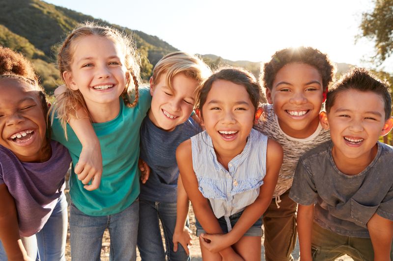 Kinder aus verschiedenen Kulturen spielen im Freien und lachen alle in die Kamera