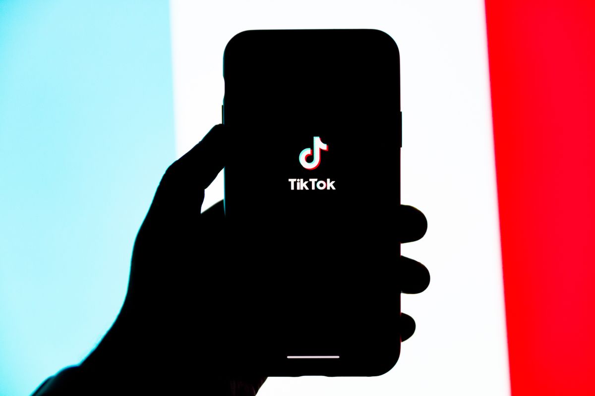 close-up of person opening tiktok on phone, brand colors in background