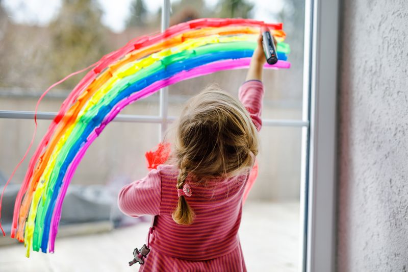 Kleinkind bemalt das Fenster mit einem Regenbogen