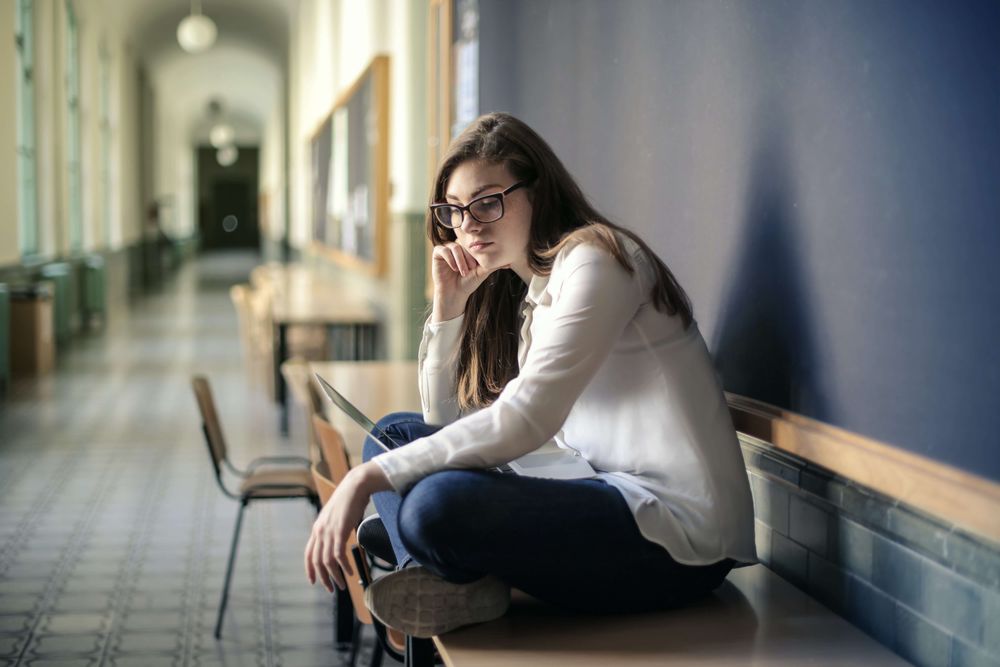 Girl sitting on a desk in a hallway, looking sad