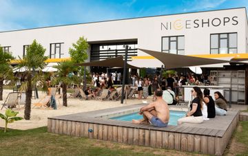 niceshops Saaz Gebäude mit Pool, Sonnensegel, Palmen, Volleyballplatz und Mitarbeiter:innen