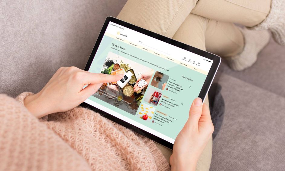 Person sitting on a couch, using a tablet, browsing an online shop with health-related products and articles.