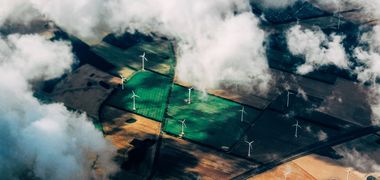 Aufnahme aus einem Flugzeug heraus von Windrädern auf Feldern, Wolken ziehen darüber, die Sonne durchbricht die Wolkendecke.
